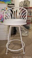 Full view of white metal bar stool with round padded seat and curved backrest with fan-like metal design.