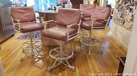 Four dusty pink upholstered swivel bar stools with metal circular footrests and painted white frames, placed on wooden floor in a kitchen