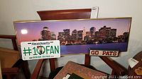 Panoramic Boston city skyline poster, Massachusetts Celtics license plate, and Go Pats sign displayed together on chairs.