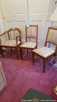 Three vintage wooden chairs (armchair and two side chairs) with striped upholstery, placed on a carpeted floor.