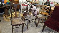 Three vintage wooden chairs grouped together: one with a caned seat, and two spindle-back chairs; wood shows water damage and scratches.