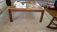 Full view of the square wooden coffee table with a glass top set on a light-colored carpeted floor.