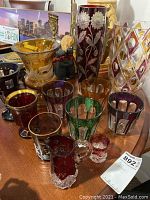 Front view of the collection showing various colors and styles of vintage cut and etched glassware, including tumblers and vases.