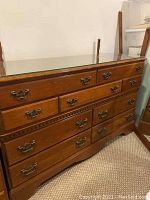 Wooden dresser with glass top and detailed metal handles, scratches visible on surface