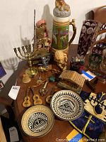 Photo showing various ethnic decor items including two bowls with geometric patterns, miniature mandolins, a signed stein, a menorah, small figurines, and a music box.