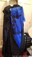 Two full-length strapless gowns hanging on a rack; one royal blue with black lace detailing, the other black with a tiered skirt. Shawls for each are also visible.