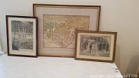 Three framed items side by side on a table: vintage map in the center, Victorian print on the right, and gazebo print on the left.