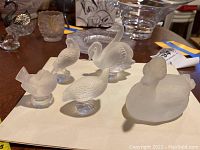 Six frosted Lalique bird figurines and one clear glass hippo on white background