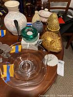 Multiple glass and pottery items on brown wood table including Simon Peirce signed bowl, Kosta Boda votive holder, vases, gold bookends, piggy bank, and sugar bowl with lid