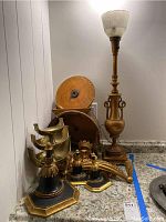 Floor lamp with glass shade and ornate brass base along with brass bowls and wooden items on countertop.