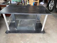 Front view of the black media stand showing magnetic glass front door and aluminum legs