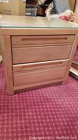 Front view of the wooden nightstand with 2 drawers and removable glass top on red patterned carpet.
