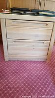 Front view of the light wood nightstand showing two drawers with carved horizontal handles and items on top.
