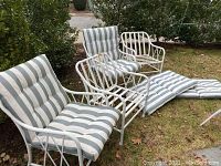 Four white metal outdoor patio chairs; two with blue and white striped cushions, two without cushions; cushions and chairs show wear; one chair missing a leg end cap.