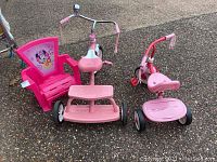 Photo of two pink Radio Flyer tricycles and a pink Minnie Mouse plastic chair on pavement.