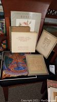 Photo of various books including vintage book 'Roses,' German art book, framed letter, and colorful starfish art print on chair.