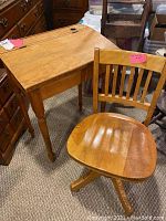 Antique wooden school desk with slant top and matching wooden chair with curved slat back, placed on carpeted floor.