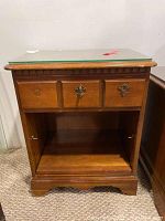 Front view of wooden side table with glass top, one drawer with decorative hardware, and open lower shelf.