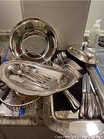 Overview photo of silver plated flatware, platters, butter dish, and wire basket arranged on countertop