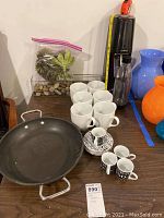 Wide view of lot showing frying pan, six mugs, four espresso cups with saucers, SodaStream machine with bottle, planter with faux succulents and natural stones