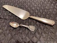 Cake server and decorative spoon placed on dark quilted fabric.