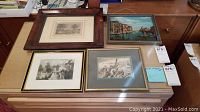 All four framed art pieces shown together on a table, two above two layout, includes a Venice canal painting and three black and white prints
