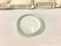 Single clear circular optical lens with smooth edges lying on a white surface.