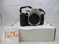 Front view of Canon EOS ELAN II 35mm film camera body with lens cover attached resting on a white box.