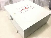 Front and side view of large white metal first aid kit case with red printing on the lid. Minor surface scratches visible.