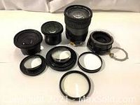 Overview photo showing eight large camera lens parts including lens barrels, rings, and optical elements arranged on white surface.