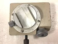 Front-angle view showing the rectangular beige metal base with circular adjustable plate, metal arms, and adjustment knobs.