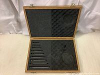 Open wooden case showing 10 driver tools arranged inside foam padding with cutouts shaped to fit them and micrometer space.