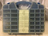 Front view of the blue plastic storage case with multiple compartments filled with anchors, screws, hooks, nails, and other picture hanging hardware components. The translucent lid displays the contents and central label.