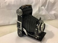 Side view of the vintage Belfoca Belca folding camera showing the extended bellows and lens assembly with focusing mechanism and silver dials.
