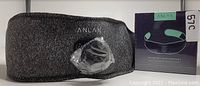 Photo of the dark grey Anlan EMS ABS belt laid flat showing the device wrapped in plastic attached to the belt and the original boxed packaging beside it