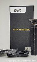 Photo of black professional hair trimmer with T-blade and textured metal tube, black USB charging cable, five black plastic attachment heads, and black box labeled HAIR TRIMMER.
