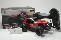 Red DEERC 9604E remote control dune buggy with black wheels and off-road tires, black ergonomic remote controller, battery charger, rechargeable battery, and original box shown together.