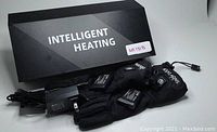 Pair of black Intelligent Heating Gloves labeled 'SNOW DEER' alongside a black box labeled 'INTELLIGENT HEATING' and a charging adapter with cables.