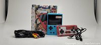 Blue handheld game console with 3 inch TFT screen, red and black wired controller, and black audio/video RCA cables.