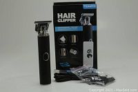 Photo showing black T-Blade hair clippers, five attachments sealed in plastic bags, micro USB charging cable, and original box
