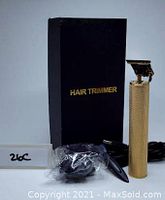 Photo showing gold look hair trimmer with textured grip, power cord and accessories in plastic wrap, with black box labeled 'HAIR TRIMMER'