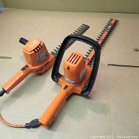 Overview photo showing two orange Black & Decker electric hedge trimmers with attached cords, one with a black handle guard by the blade.