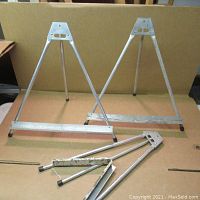 Photo of three metal folding easels standing and one folded, showing overall condition and size.
