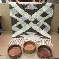 Full view of three teak bowls in front of wool hanging with geometric design