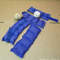 Photo showing two purple ankle weights, two smaller wrist weights, and two white baseballs placed on cardboard background.