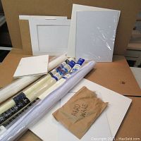 Lot contents showing stacked white canvases and panel boards alongside rolls of cotton cross stitch fabric and rolled paper, brown envelope labeled 'hardware' visible.