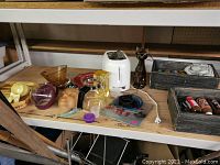 Photo showing a variety of vintage and used household items including a white toaster, a decorative ceramic cat figurine, a ceramic face mask, glass bowls, a clear coffee pot, and some painted tiles.