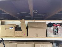 Shelf with several cardboard boxes including one labeled 'Christmas Lights Gift Wrap' and a clear plastic bin with wool blankets inside