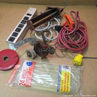 Box of assorted individual hand tools including pipe cutter, hand cranks, red extension cord, outlet strip, spool of cable ties