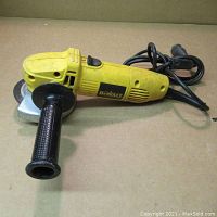 Full angle grinder with attached side handle and power cord coiled behind.